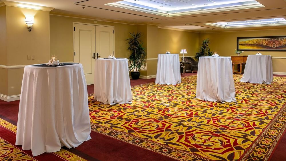 White cocktail tables by a wooden dresser on a patterned rug in Capitol Ballroom at Warwick Denver