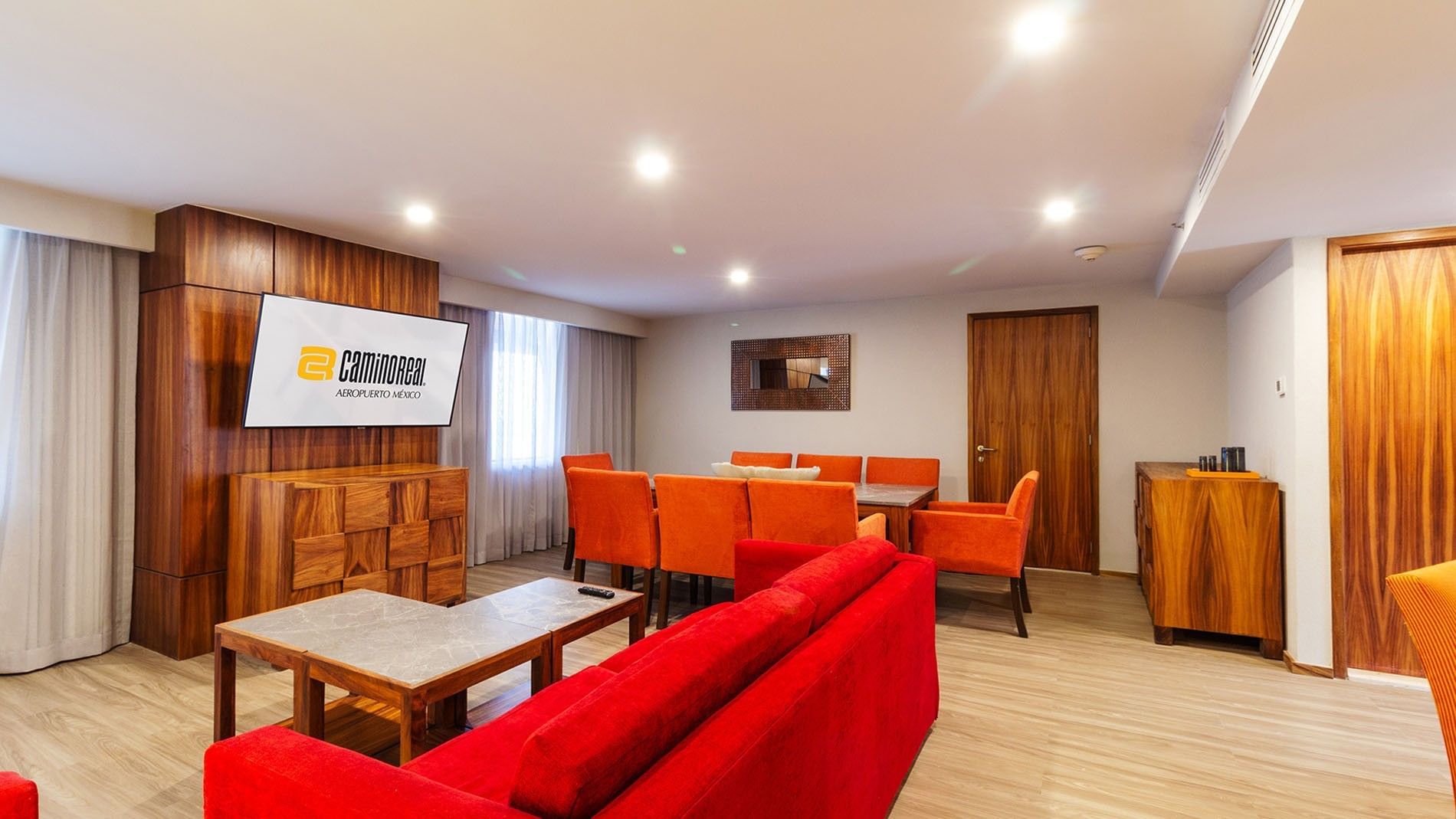 Salón elegante con sofá rojo y mesa de comedor en Master Suite King de Camino Real Aeropuerto México en Ciudad de México