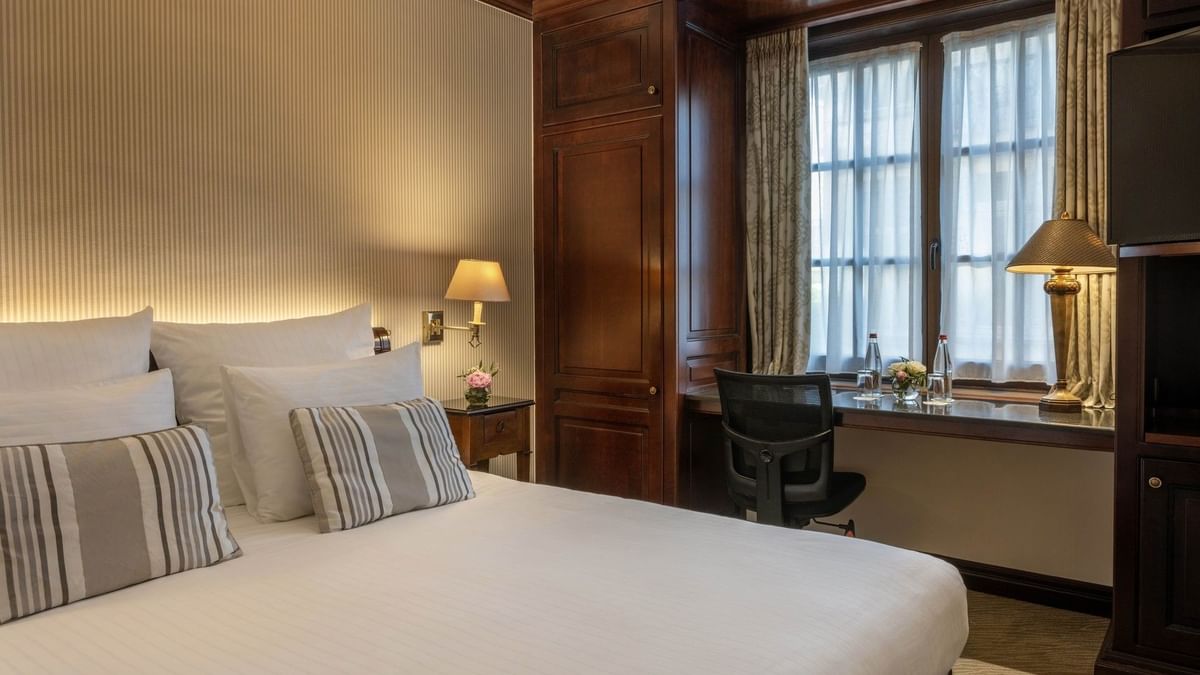 Bed with a wooden cupboard and a working desk near window in Classic Room at Warwick Grand Place Brussels