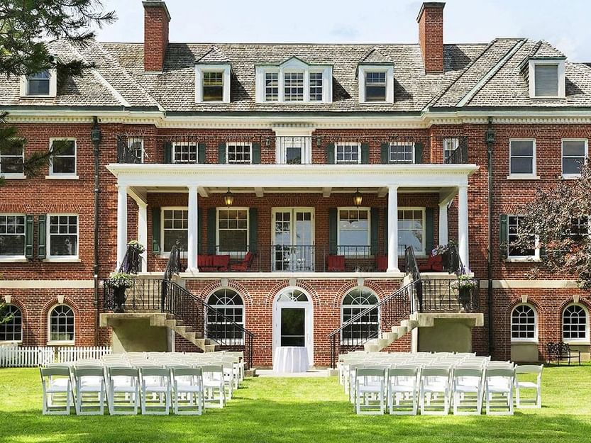 White chairs arranged on a grassy lawn for a ceremony outside the brick Spencer Hotel & Conference Centre