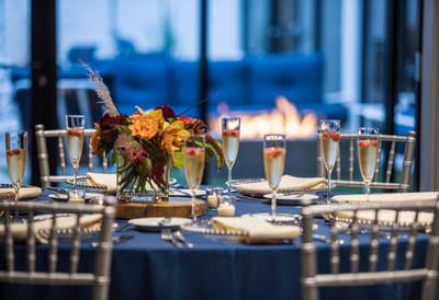 Round table setting featuring champagne flutes & floral arrangements near a fire pit at Sable Oaks Weddings and Events