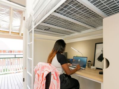 Student working on a laptop at a desk under single loft bunk at UniLodge Herston room.
