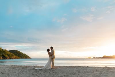 Newlyweds embracing on a wide sandy beach during a bright, beautiful sunset by the ocean at Emerald Beach Resort