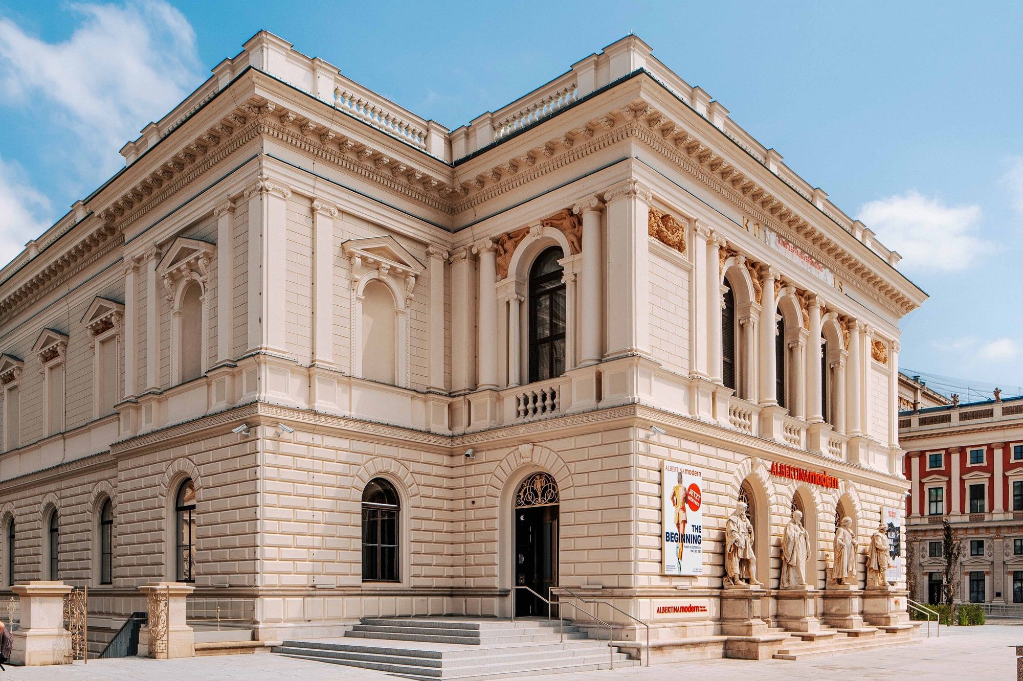 Historic exterior view of Albertina modern in Vienna featuring neoclassical architecture, columns, and sculptures at the museum entrance