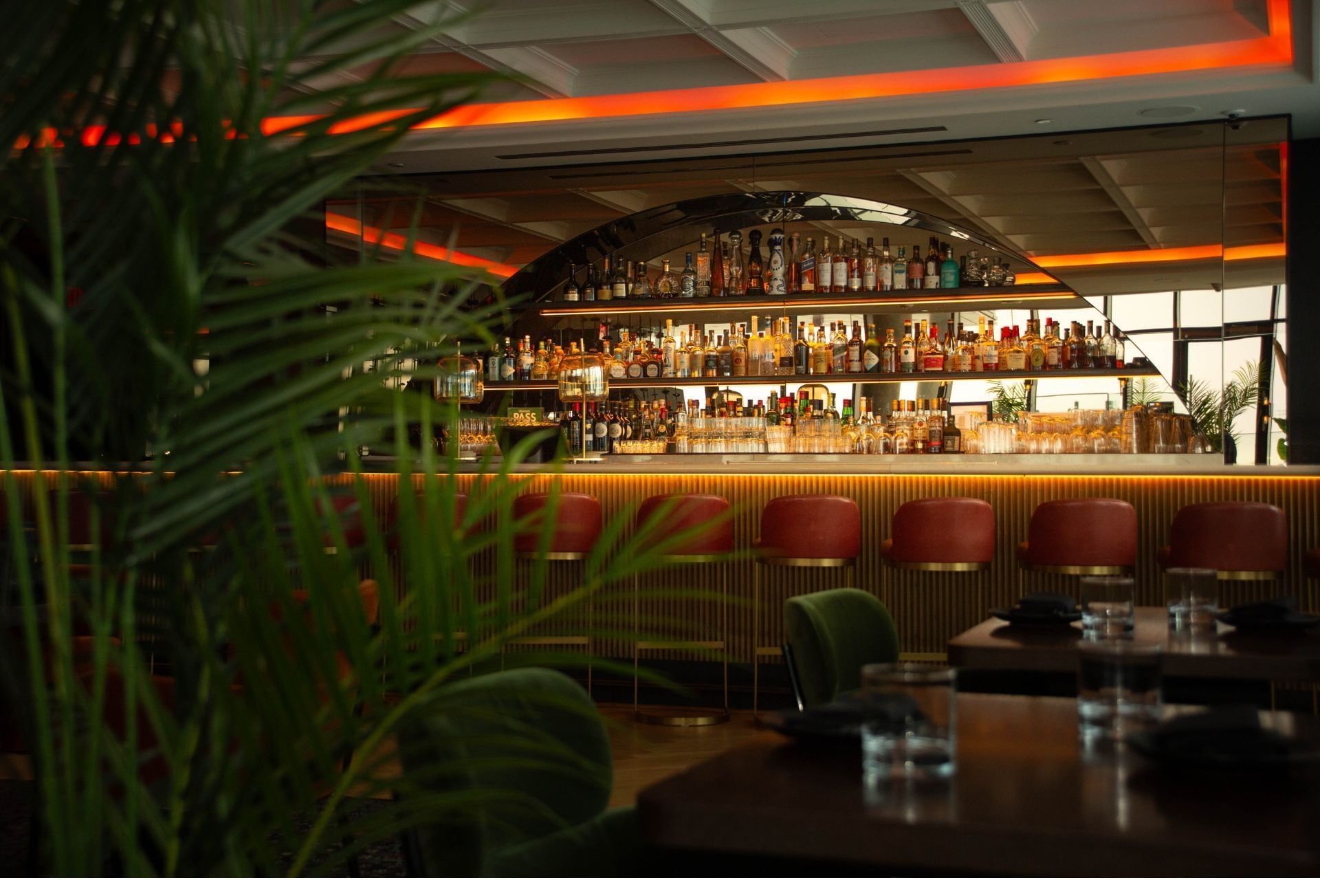 Dimly lit bar with red leather stools facing illuminated liquor shelves and dining tables at Hotel X Toronto