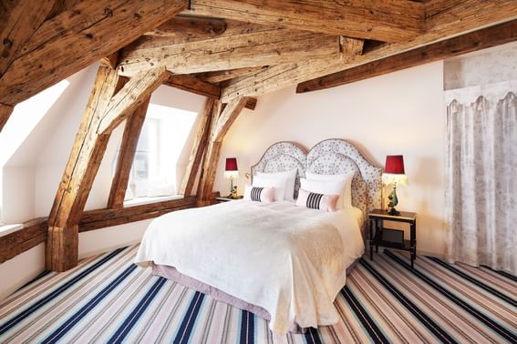 View into the spacious room in the attic of the hotel in Vienna  furnished with a cozy double bed under old wooden beams