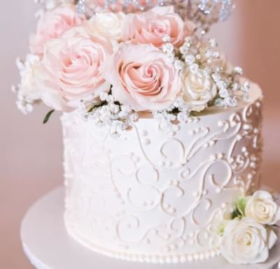 Close-up of a white wedding cake with pink and white roses by scrollwork icing at The Glenmore Inn & Convention Centre