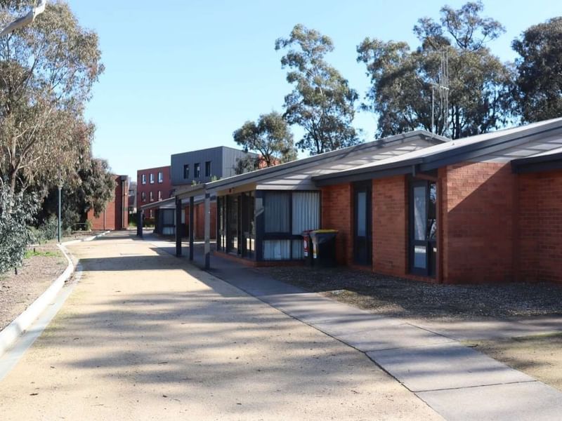 Row of brick buildings with flat roofs and glass doors, lined with trees on a sunny day.