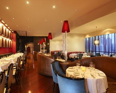 Round dining tables with curved leather banquettes and tall red lampshades in the restaurant at Megapolis Hotel