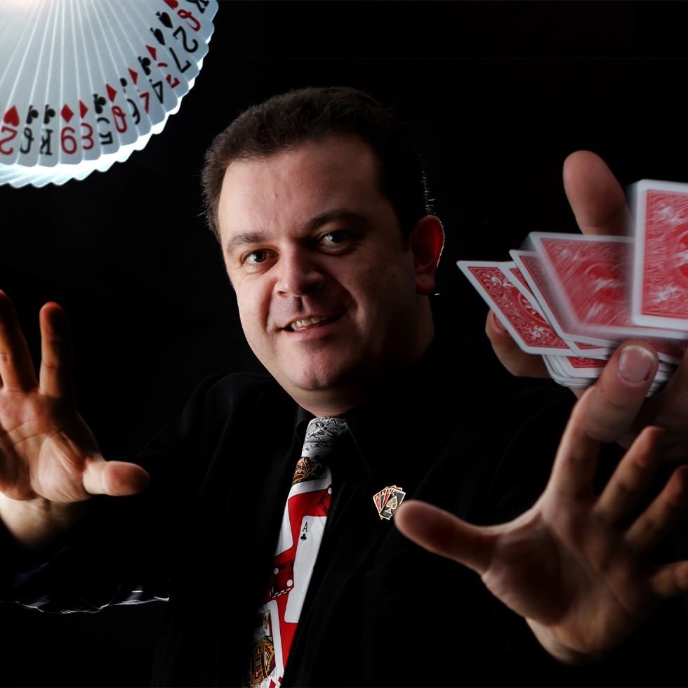 Smiling magician performing a magic show with playing cards in his hands.