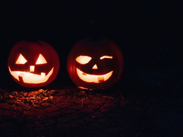 Two carved jack-o\'-lantern pumpkins glowing brightly in dark outdoors during Halloween at Shangri-La Resort and Golf Club