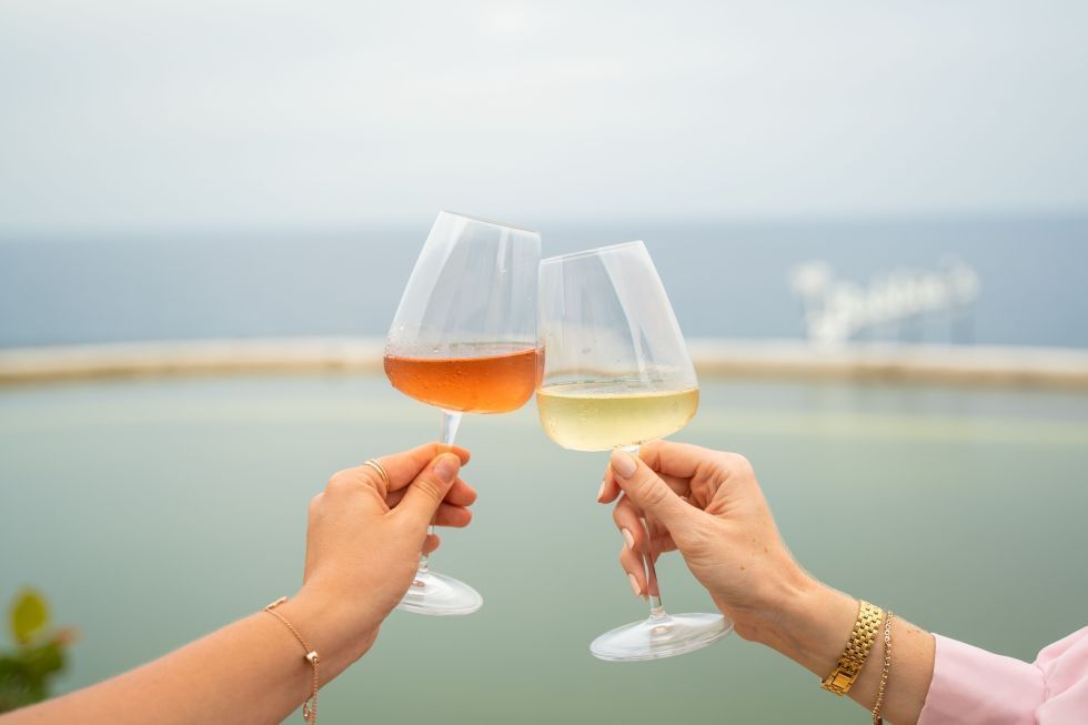 Twee handen klinken glazen rosé en witte wijn tegen een serene oceaanachtergrond bij Golden Rock Resort