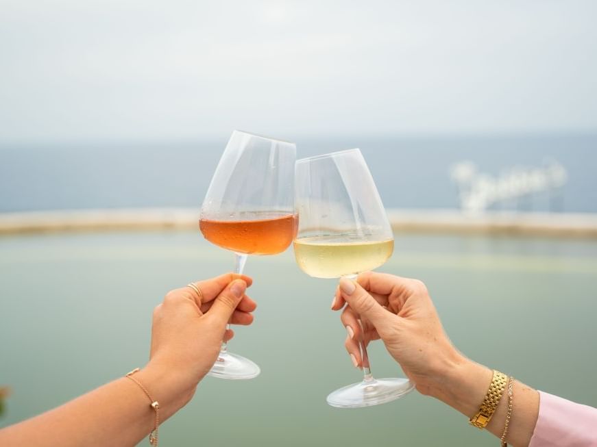 Two hands clink glasses of rosé and white wine against a serene ocean backdrop at Golden Rock Resort