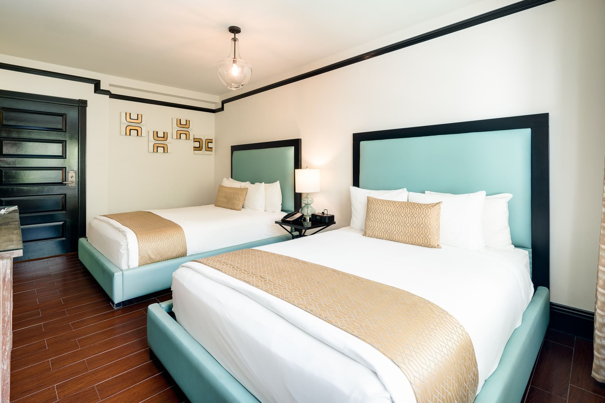 A hotel room with two beds, white walls, and dark wood flooring.