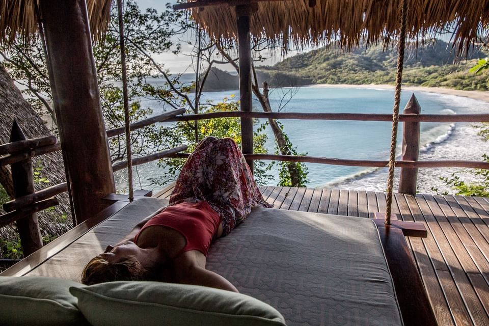 Guest relaxing on a hanging daybed overlooking the private bay at Morgan’s Rock Reserve & Ecolodge
