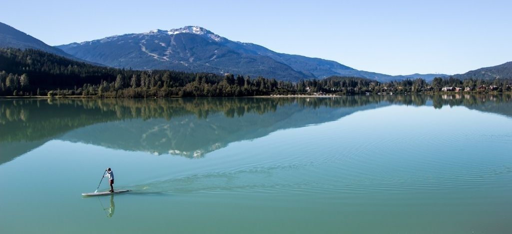 Person paddleboarding on a calm Whistler lake surrounded by mountains.