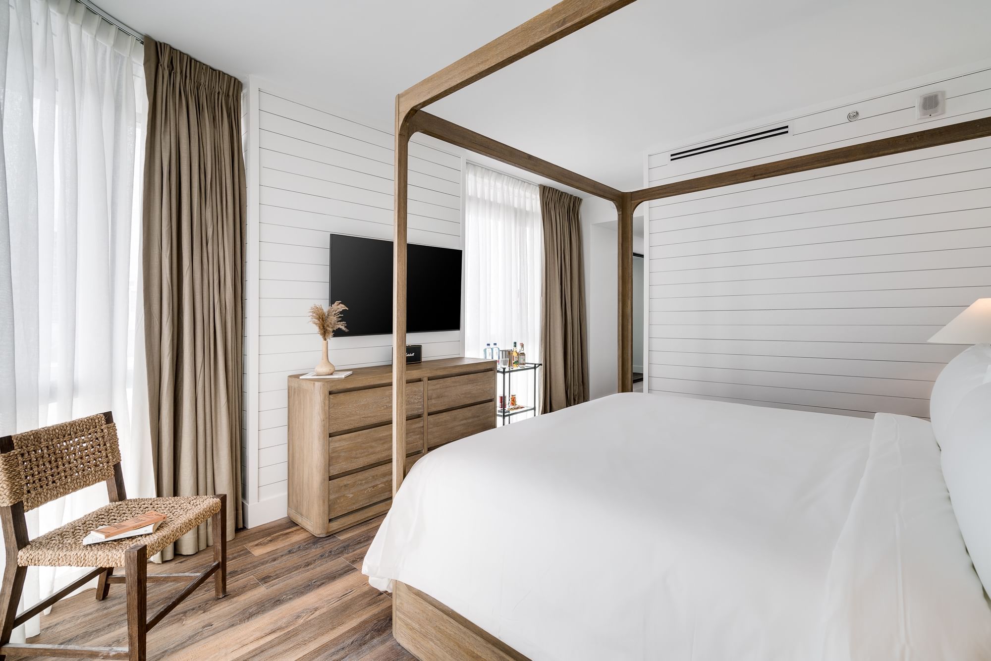 A clean and modern guest room with a four-poster bed, wooden furniture, and a shiplap wall.