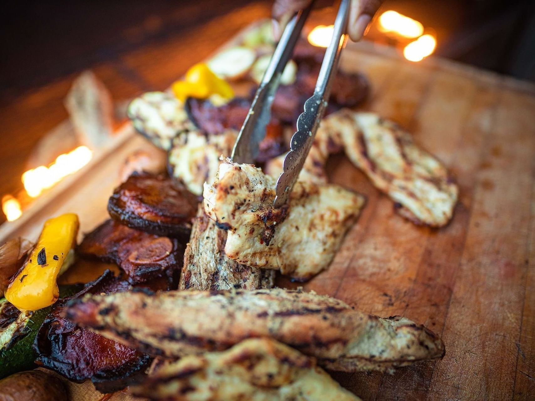 Tongs lifting freshly grilled chicken breast from a wooden serving platter at the Jamaica Pegasus Hotel