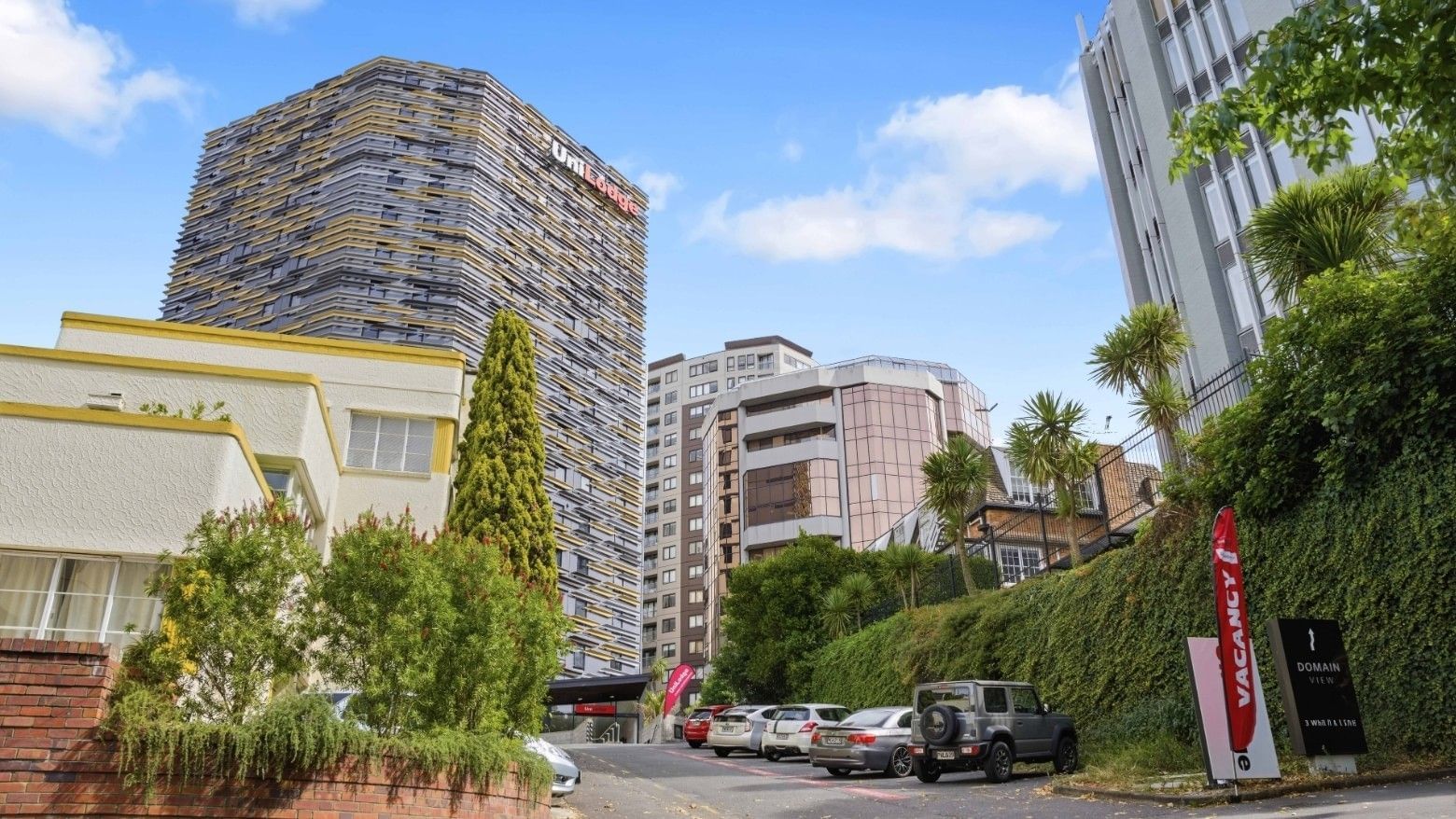 UniLodge Auckland City building with cars parked outside on a sunny day.
