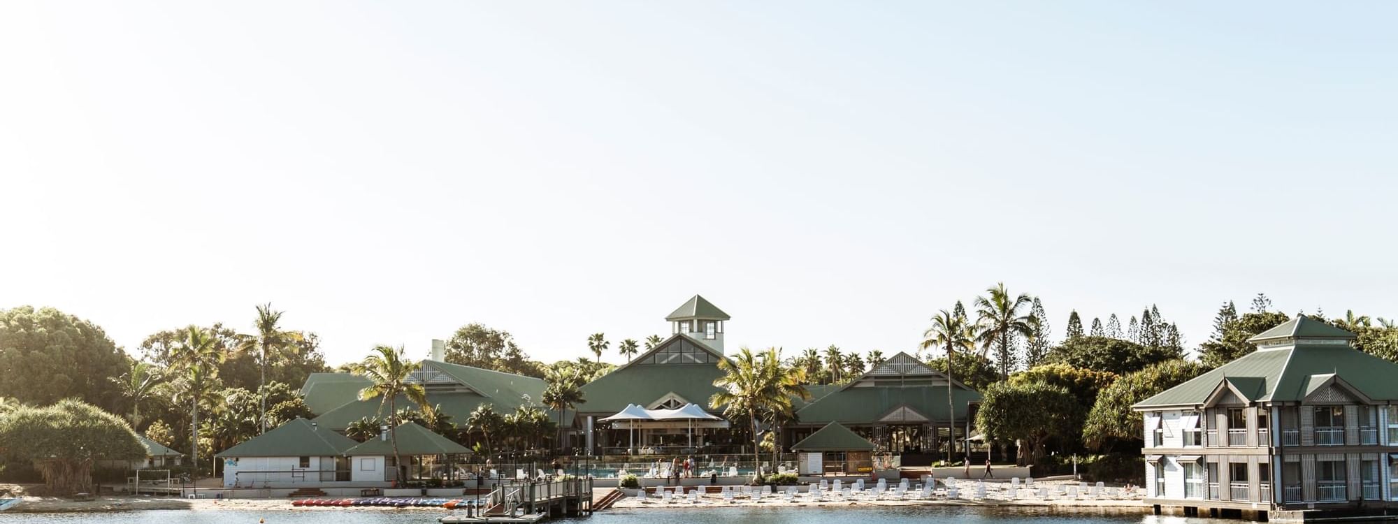 Novotel Sunshine Coast Resort with green roofs by a calm lagoon surrounded by palm trees and sun loungers