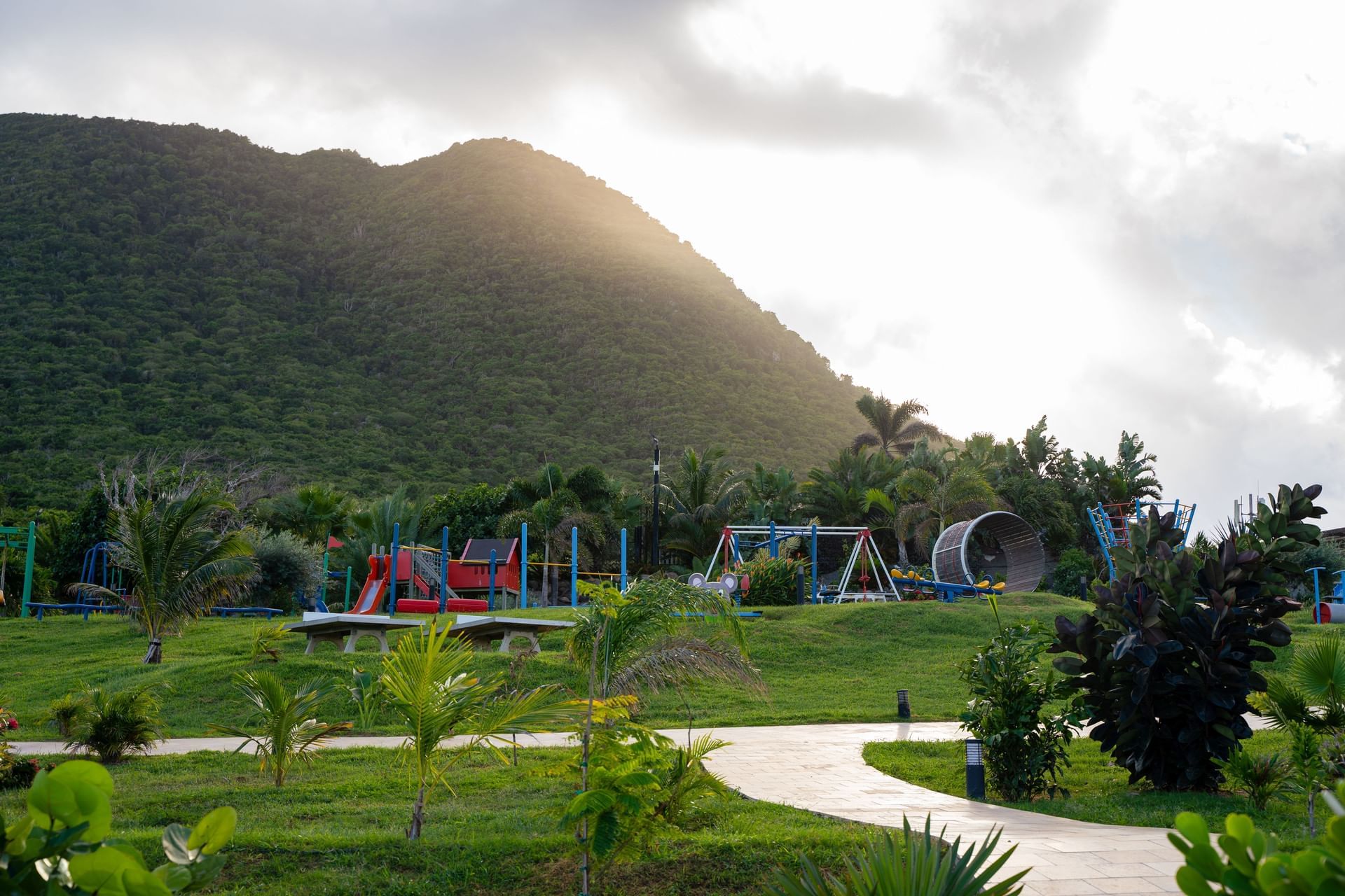 Vibrant playground with swings and slides, surrounded by lush greenery and a mountain at Golden Rock Resort