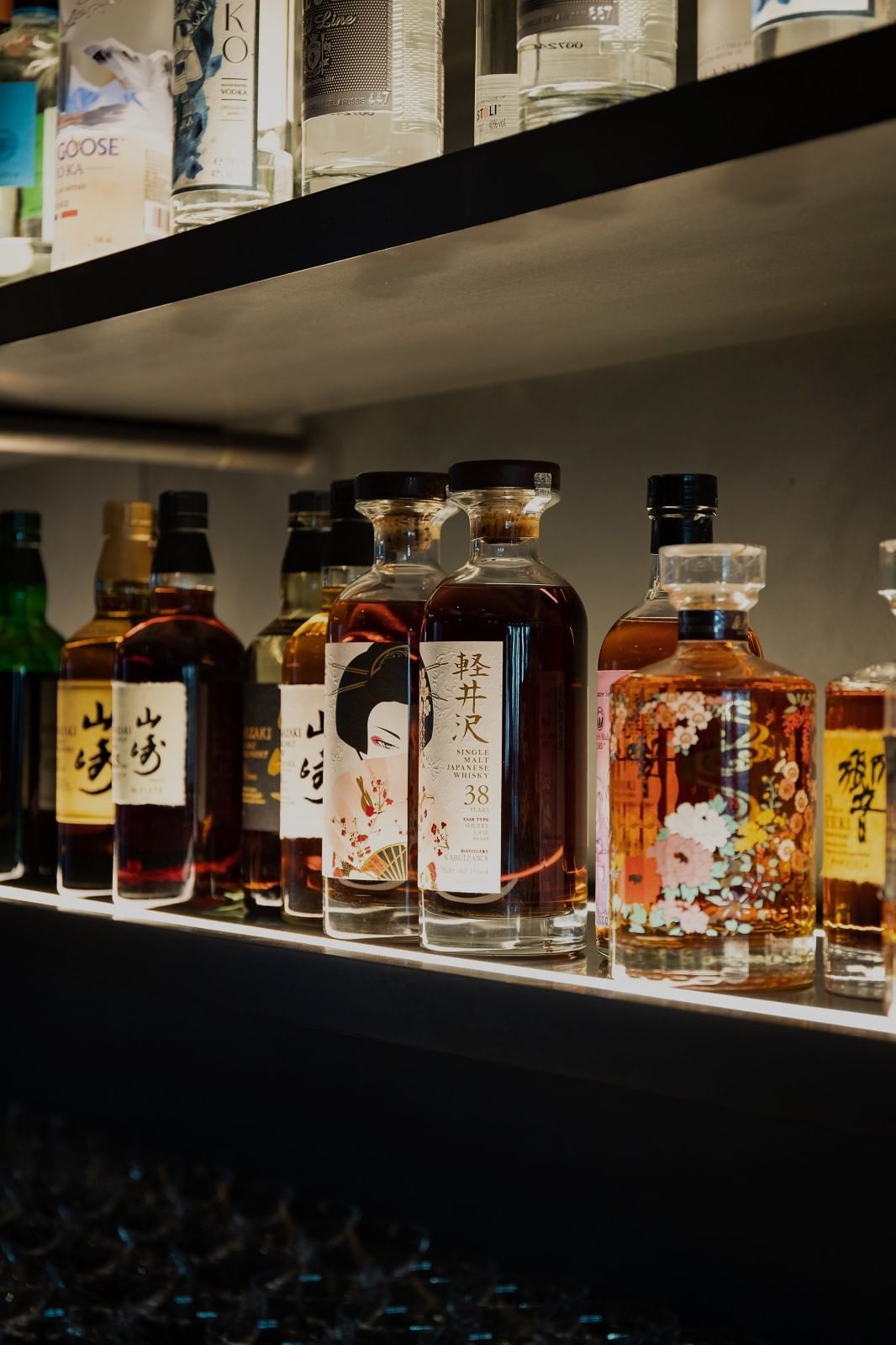 Various beautifully designed and labeled liquor bottles displayed on a well-lit shelf at The Londoner Hotel