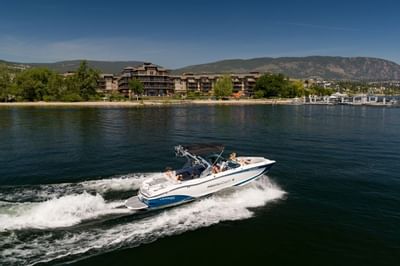 People riding on a boat in the lake near the resort and mountain under blue sky.