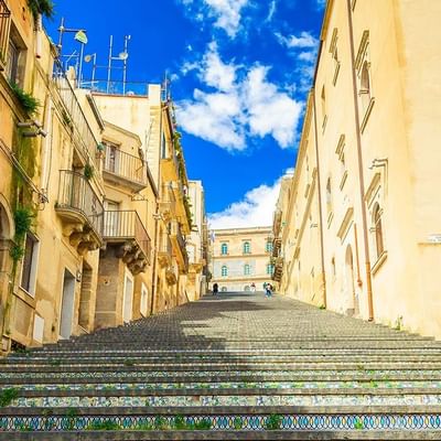 Blick auf eine breite Treppe in einer schmalen Straße zwischen alten Gebäuden unter einem blauen Himmel.