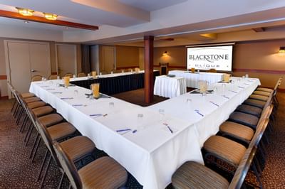 U-shaped table with a projector screen and carpeted floors in the Meeting Room at Blackstone Mountain Lodge