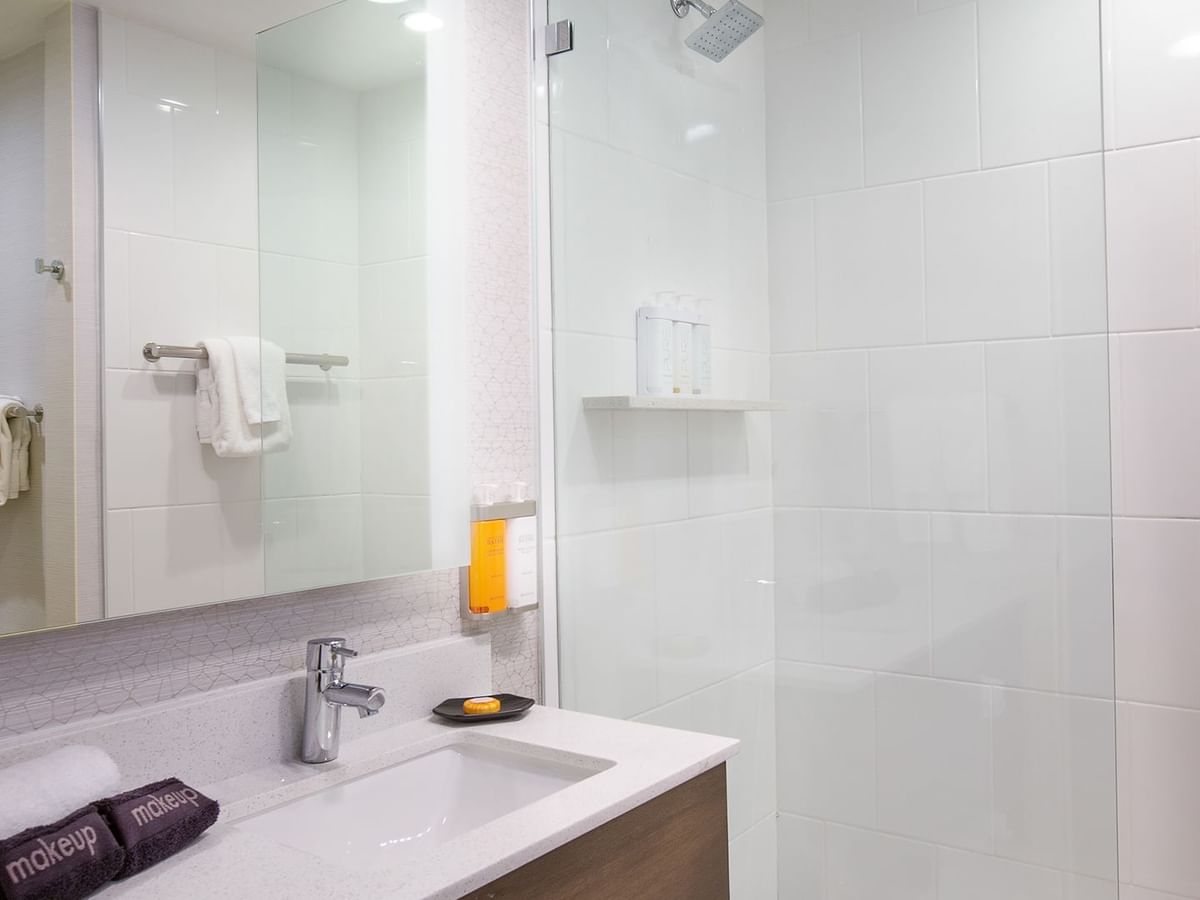 Modern bathroom with white tiles, a mirror, sink, towels, and shower enclosure.