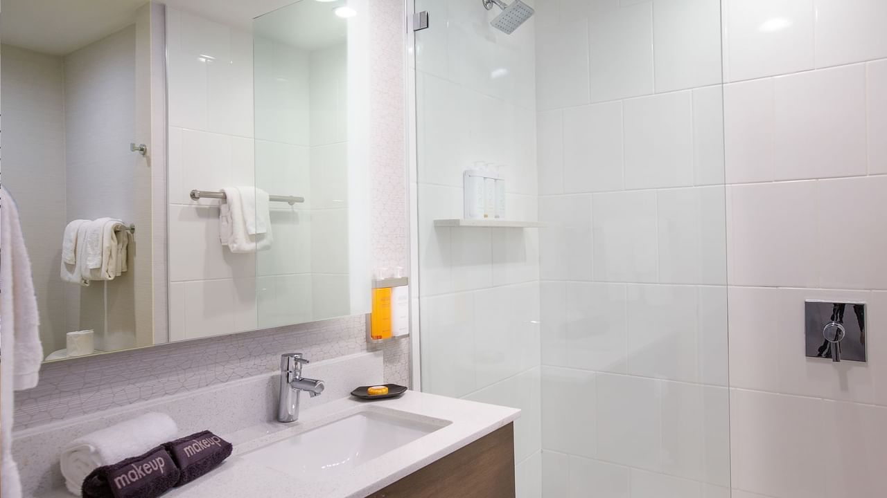 Modern bathroom with white tiles, a sink, a mirror, a shower stall, and towels.