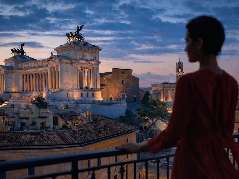 Woman in dress standing on balcony overlooking historic city landmark in Lyve Rooftop Terrace at the Thompson Rome