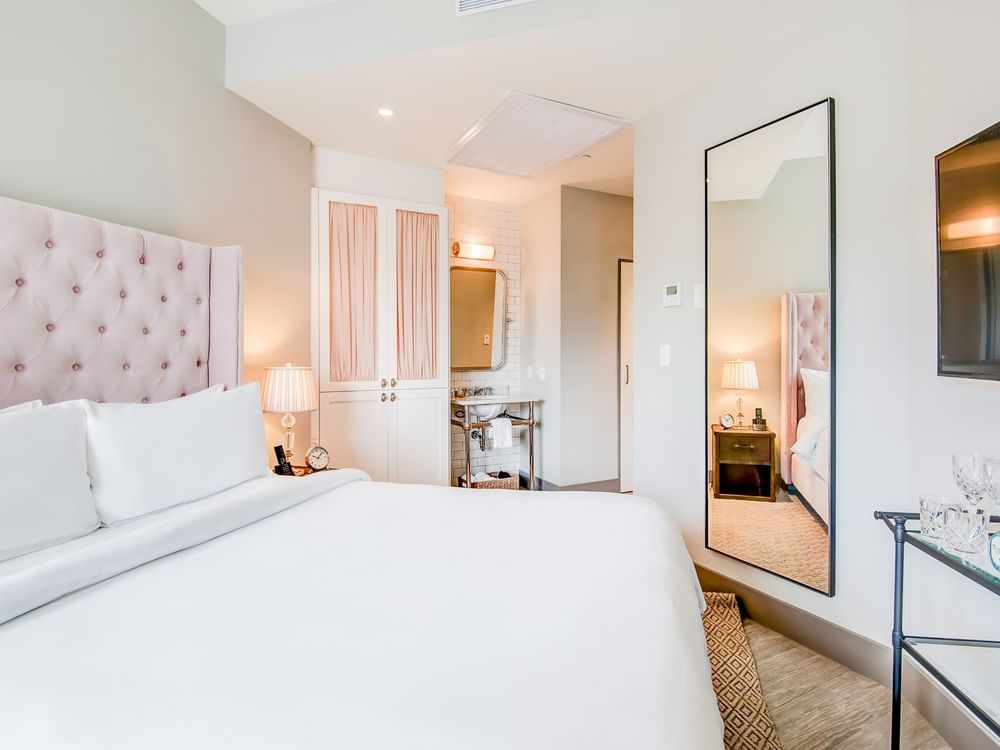 A wide view of a hotel room with a king-sized bed, a large mirror, and a nightstand.