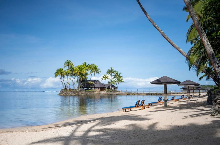 Beach with lounge chairs and umbrellas on a sunny day at Warwick Fiji Resort and Spa.