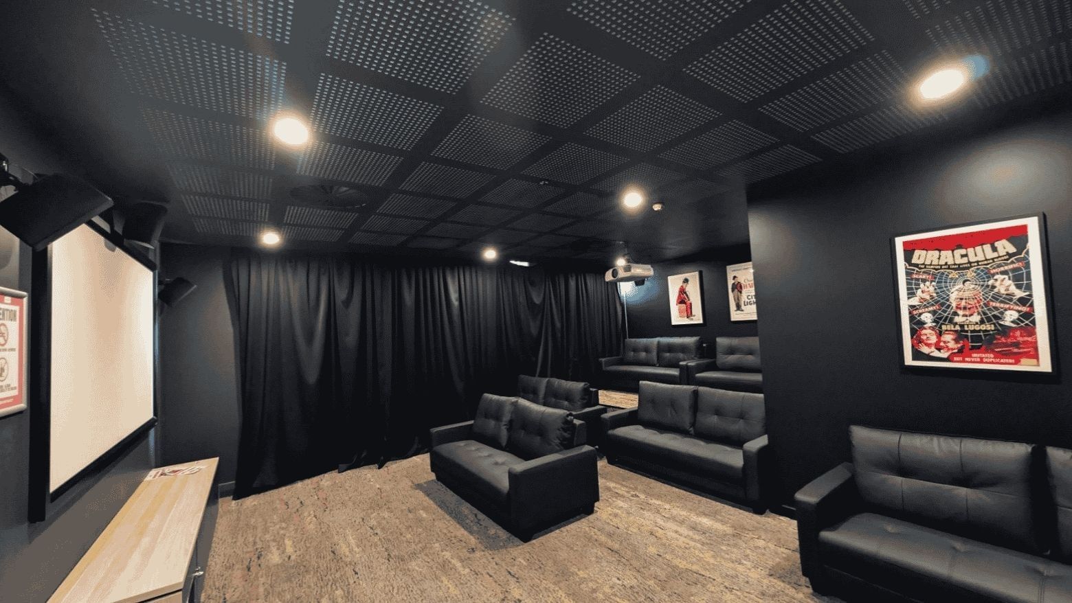 Modern cinema room with black leather seating, projection screen, and vintage movie posters at UniLodge Herston