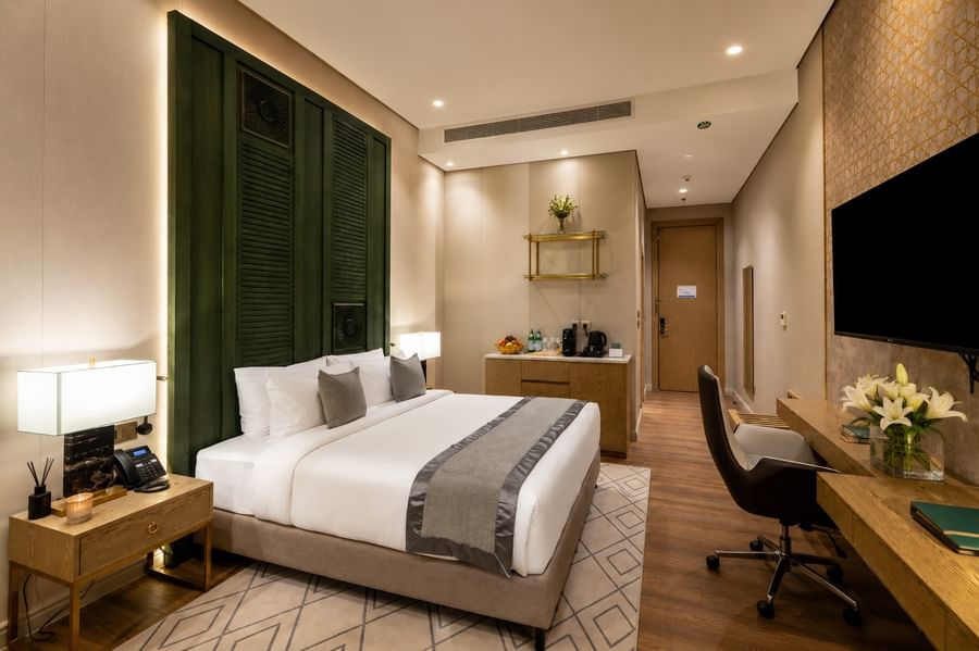 King bed facing wall TV beside desk in Deluxe Room at Naviti by Warwick Jeddah, featuring spacious hotel rooms in Jeddah