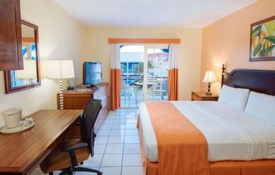 Superior Room King featuring a king bed, desk, TV, and balcony with pool view, adorned with warm accents at Bay Gardens Inn