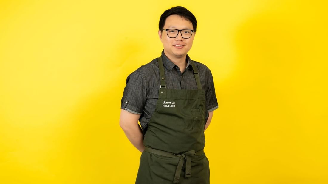 Chef Jiun An Lin standing confidently in front of a bright yellow background at Novotel Sydney Olympic Park