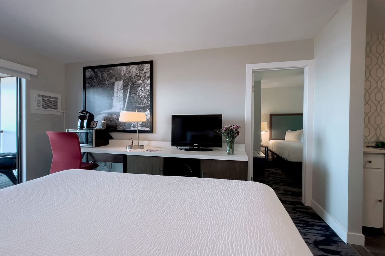 A guest room with king bed, tv, chair, desk, lamp, fridge, microwave, patio doors