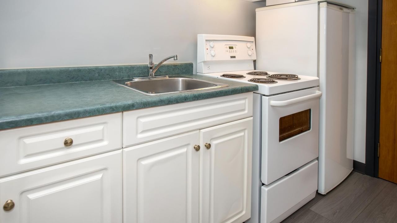 White kitchen with a fridge, stove, sink, and cabinets with teal countertops.