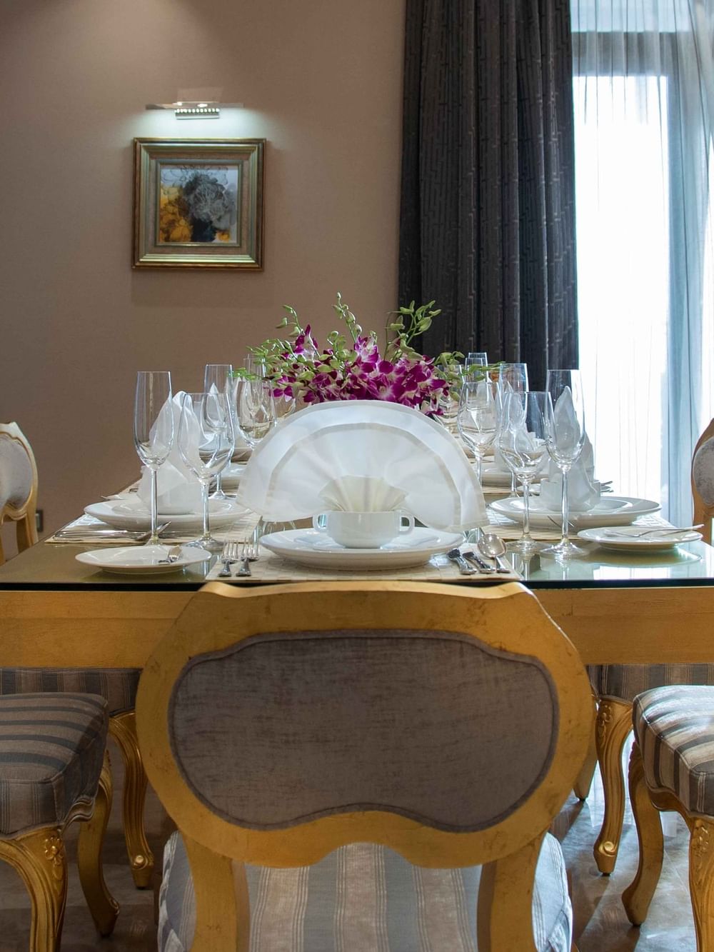 Dining table with glassware by gold-trimmed chairs under a floral centerpiece in Penthouse Villa at Warwick Al Khobar