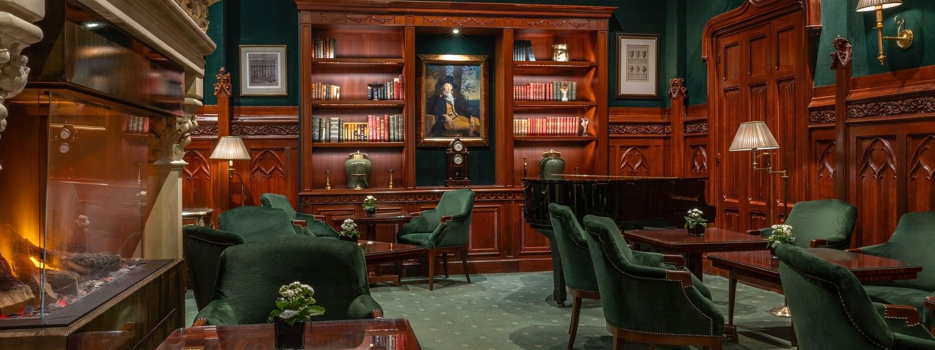 Green velvet chairs by wooden tables surrounding a grand piano and bookshelf under dark walls at Warwick Hotels & Resorts
