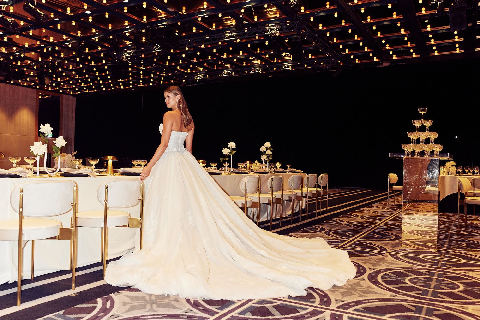 Woman in a white strapless gown standing in front of a dining setup in an event space.