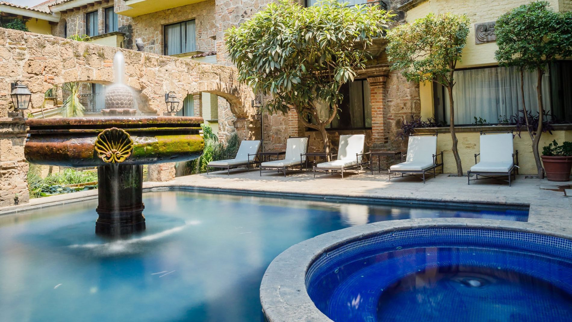 Outdoor pool area with a stone fountain and white lounge chairs at Quinta Real Guadalajara