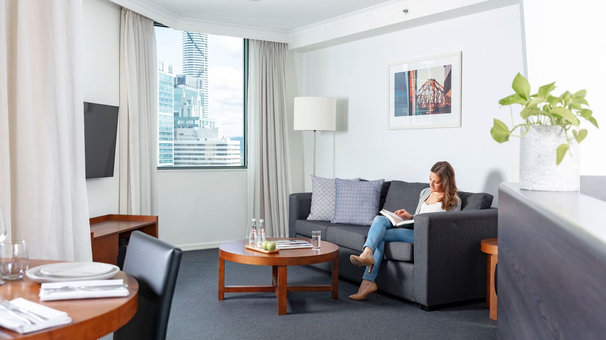 A woman relaxing and reading a book on a sofa in Premium One Bedroom Apartments with a window view at The Sebel Brisbane