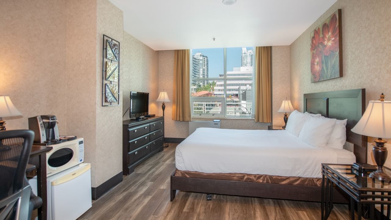 Coast Queen room with a queen bed, nightstands, desk, fridge, coffee maker, and window at Coast Lonsdale Quay Hotel