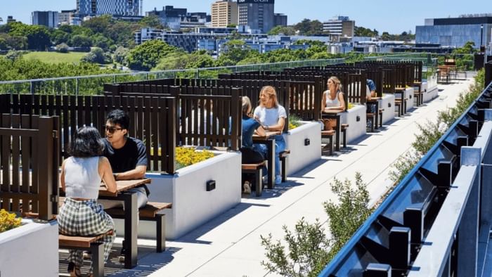 People sit at tables on a rooftop terrace with a view of a city skyline.