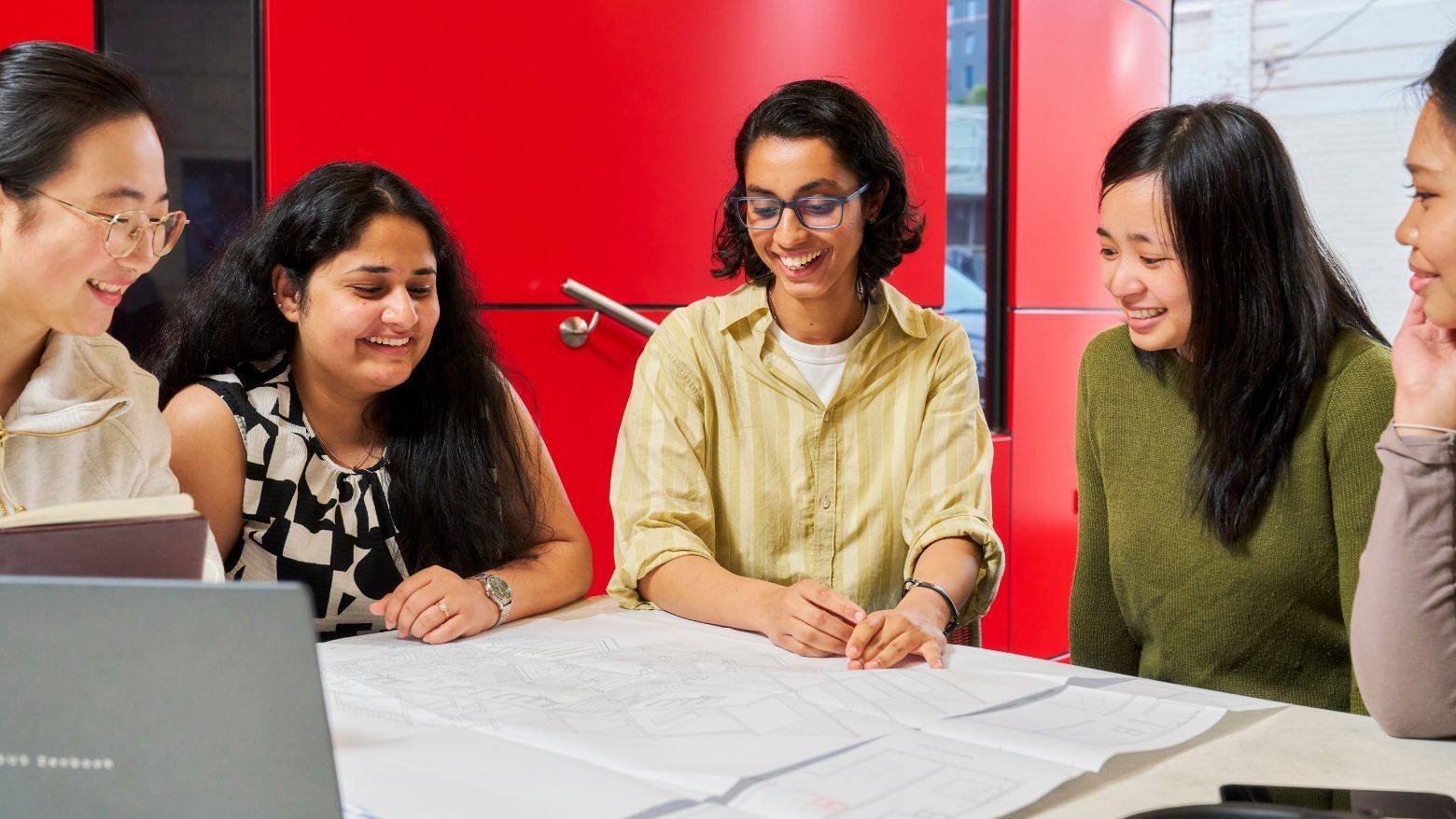 Residents smiling and looking at a project around a table with a laptop at Student Living D2.