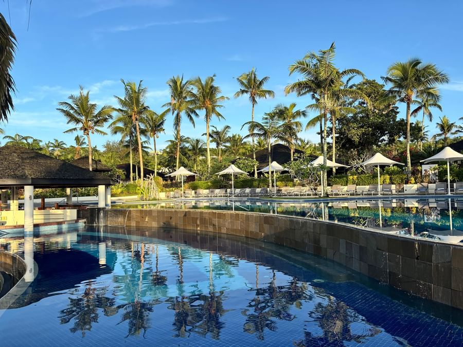 Swimming pool with blue water and lounge chairs under umbrellas at Warwick Le Lagon.