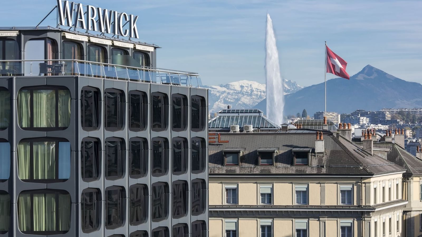 Modern Warwick Geneva Hotel exterior by the Jet d'Eau fountain under snowy mountains